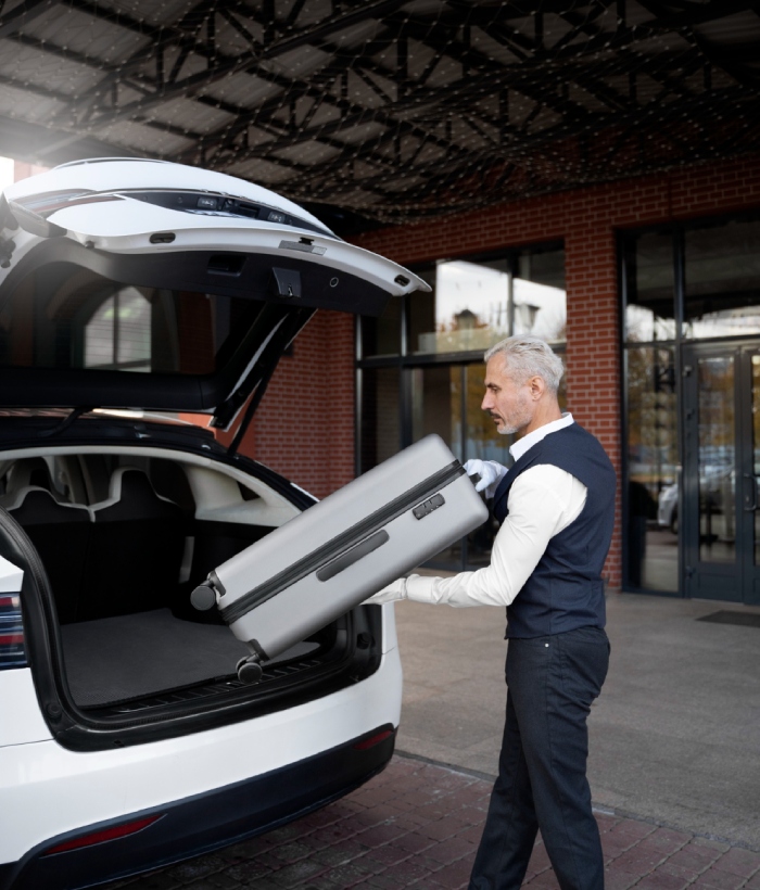 Chauffeur chargeant une valise dans un véhicule pour un transfert aéroport