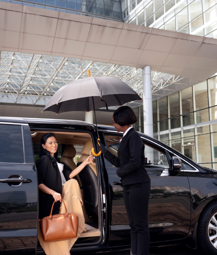 Chauffeuse accueillant une passagère avec parapluie pour un transport événementiel